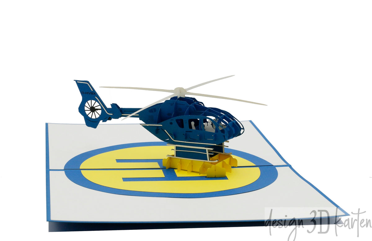 Aufgeklappte Pop-up-Karte mit einem blauen Hubschrauber auf einem gelb-blauen Landeplatz.