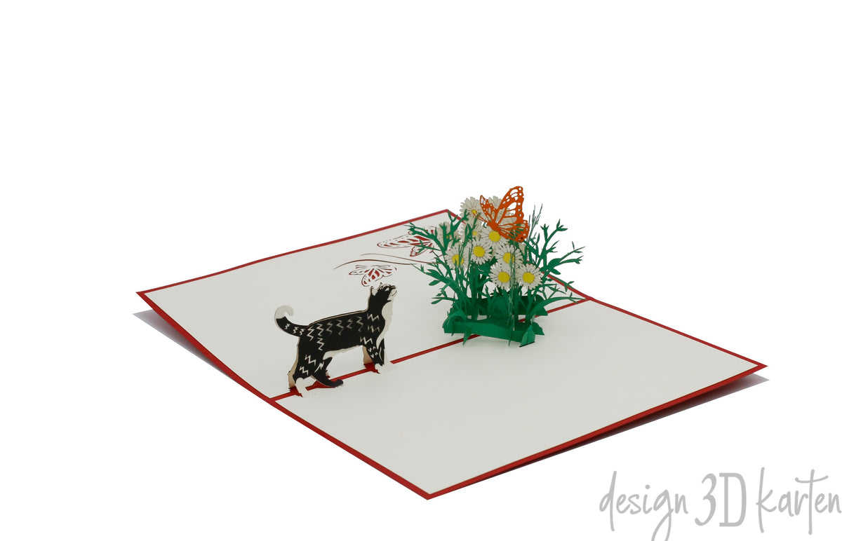 Aufgeklappte Pop-up-Karte mit Katze, Margeritenwiese und Schmetterling, schräg von oben fotografiert.