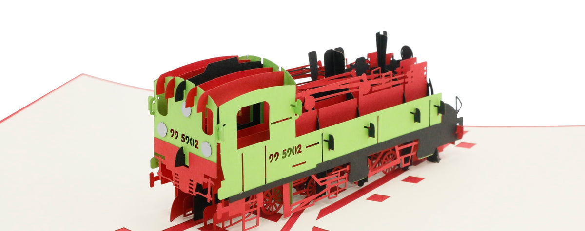 Aufgeklappte Pop-up-Karte mit einer rot-grünen Dampflokomotive auf Schienen, schräg von der Seite fotografiert.