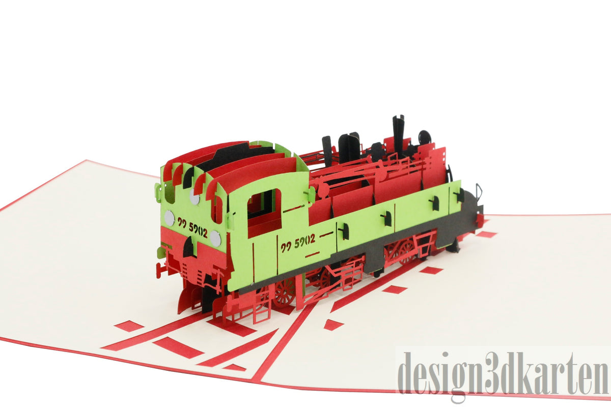 Aufgeklappte Pop-up-Karte mit einer rot-grünen Dampflokomotive auf Schienen, schräg von der Seite fotografiert.