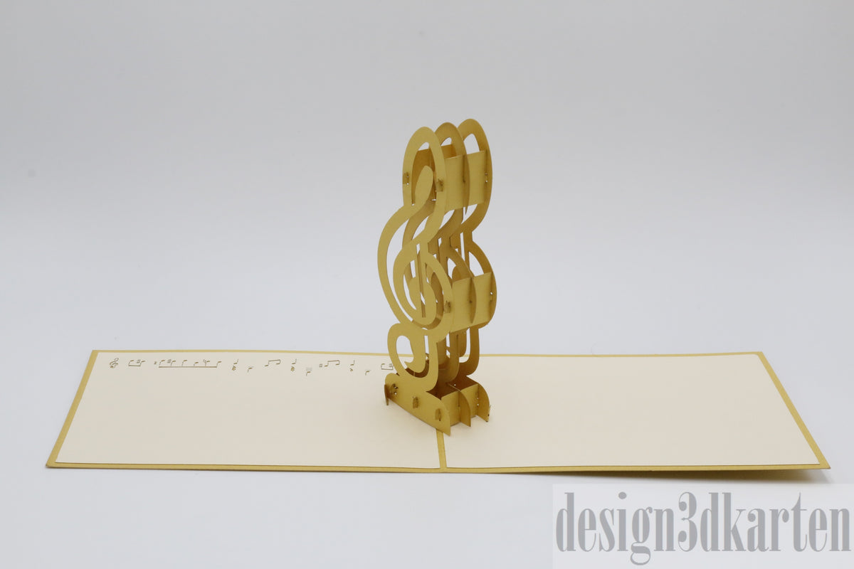 Aufgeklappte Pop-up-Karte mit einem goldenen Violinschlüssel auf einem Notenblatt, schräg fotografiert.