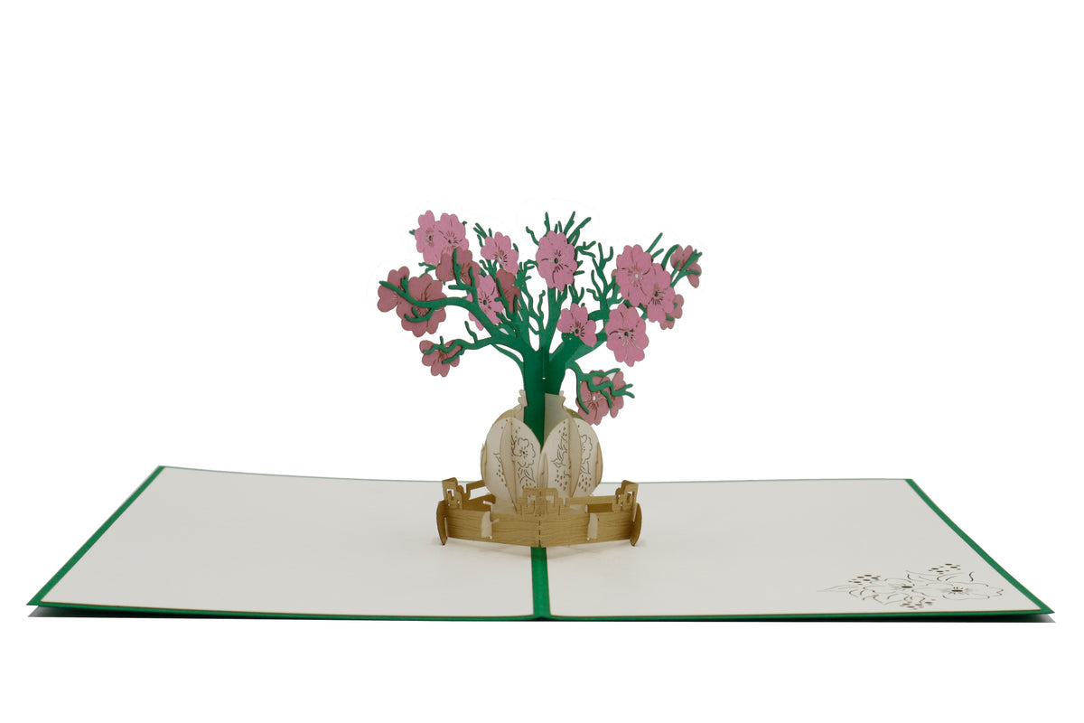 Aufgeklappte weiße Pop-up-Karte mit grünem Rand und einem Blumenstrauß in goldener Vase, seitlich fotografiert.