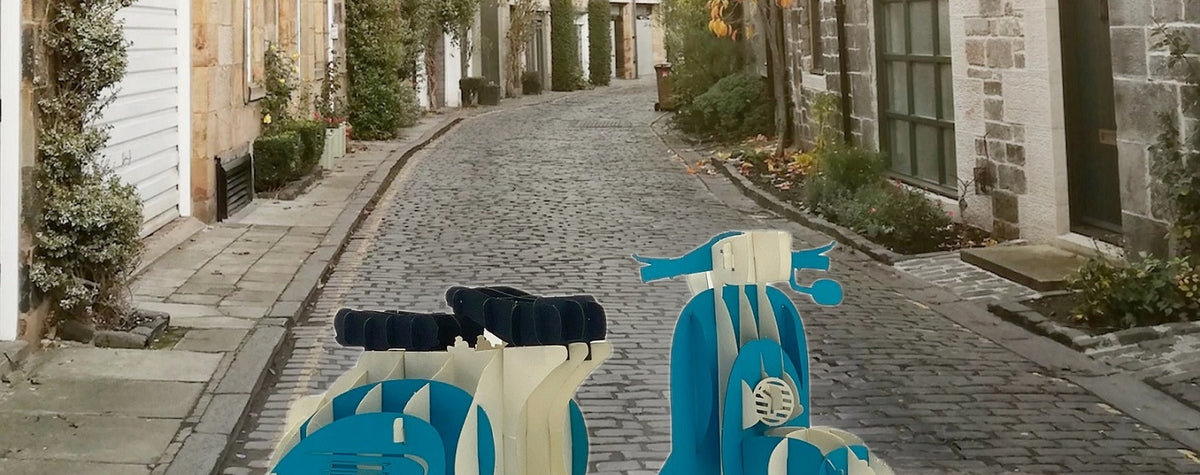 Pop-up-Karte mit blauer Vespa, aufgestellt in einer gepflasterten Altstadtgasse.