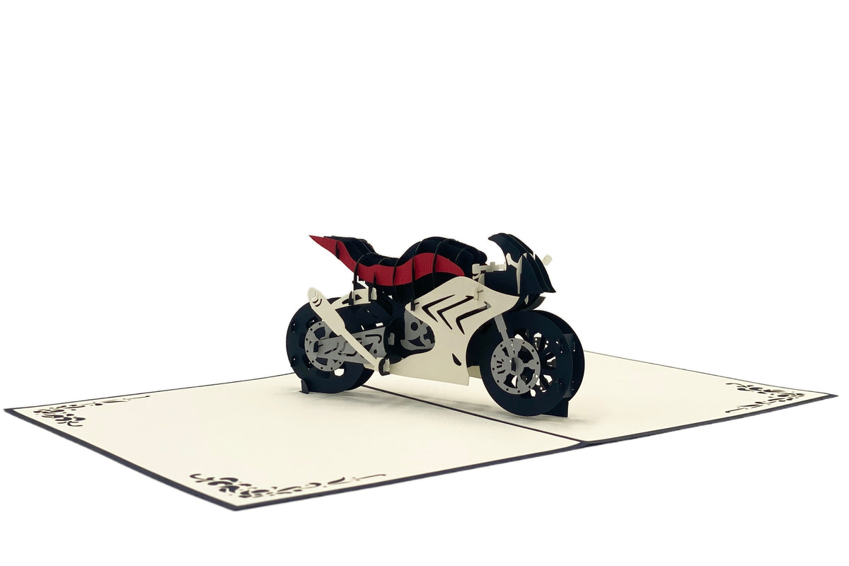 Aufgeklappte Pop-up-Karte mit einer Rennmaschine aus Papier, leicht von oben fotografiert.