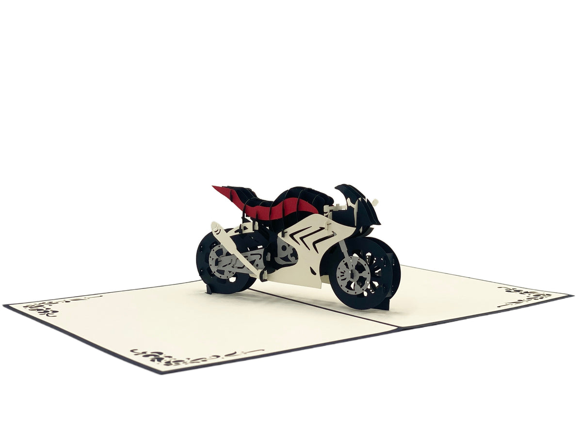Aufgeklappte Pop-up-Karte mit einer Rennmaschine aus Papier, leicht von oben fotografiert.