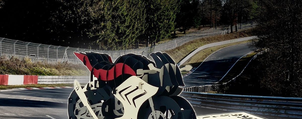 Pop-up-Karte mit Rennmotorrad, aufgestellt vor einer echten Rennstrecke mit Leitplanken und Wald.