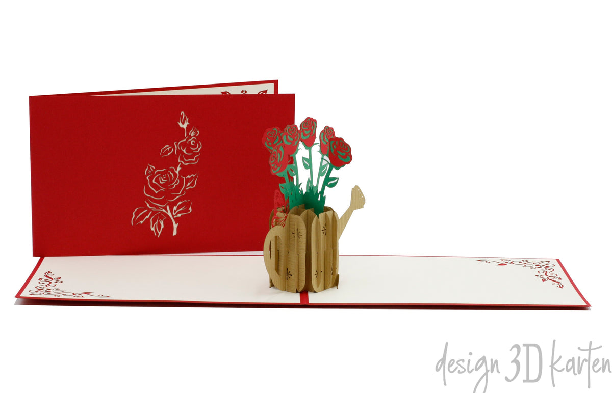 Aufgeklappte Pop-up-Karte mit roten Rosen in einer goldenen Gießkanne, dahinter die rote Kartenvorderseite mit Rosen-Scherenschnitt.