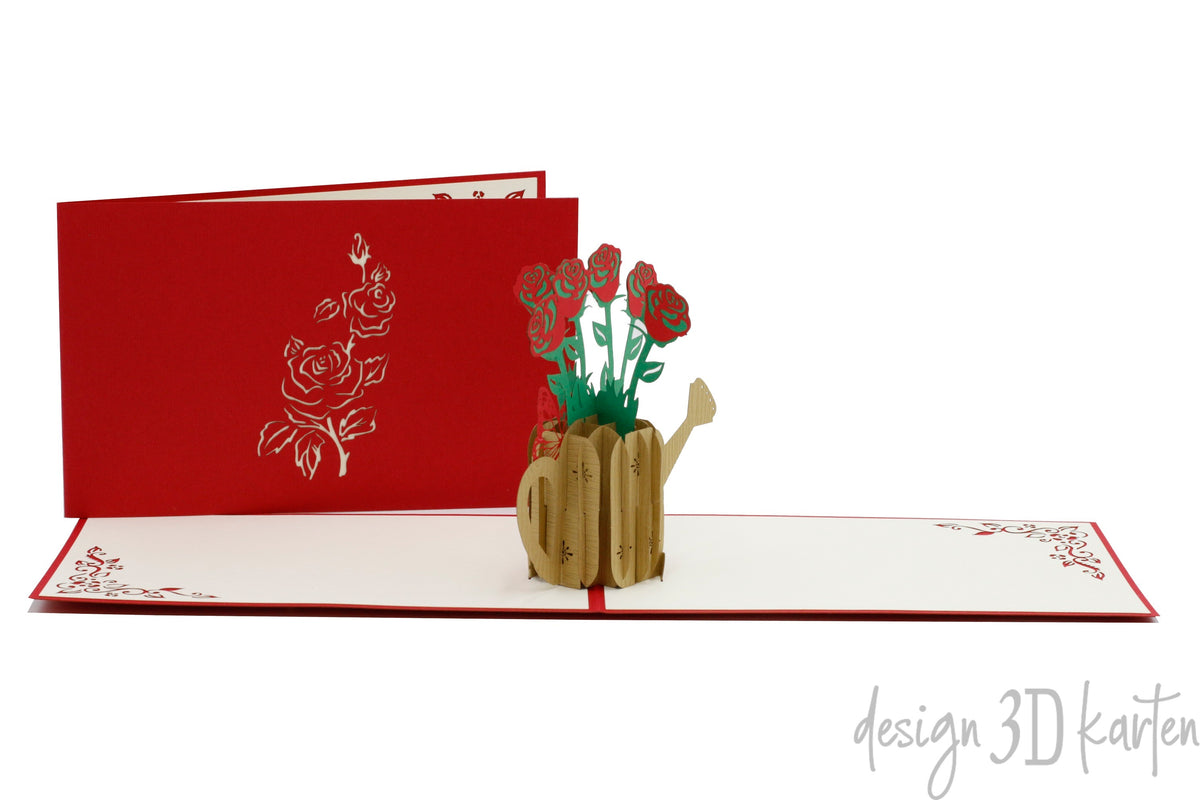 Aufgeklappte Pop-up-Karte mit roten Rosen in einer goldenen Gießkanne, dahinter die rote Kartenvorderseite mit Rosen-Scherenschnitt.