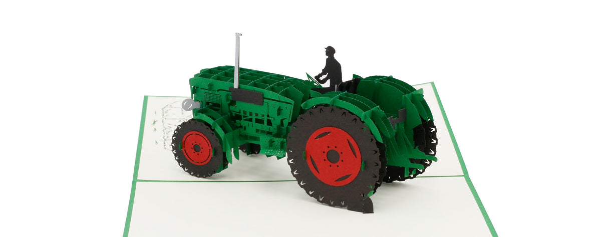 Aufgeklappte Pop-up-Karte mit grünem Oldtimer-Traktor und Fahrerfigur, schräg von oben fotografiert.