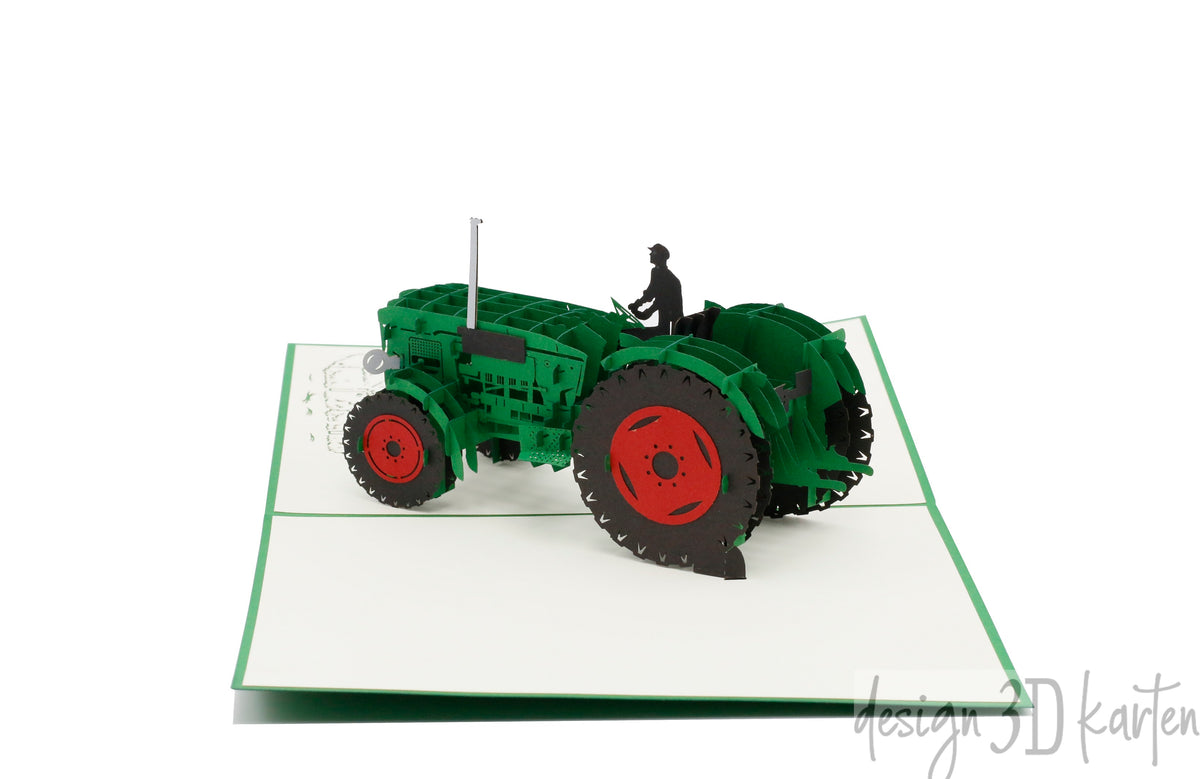 Aufgeklappte Pop-up-Karte mit grünem Oldtimer-Traktor und Fahrerfigur, schräg von oben fotografiert.