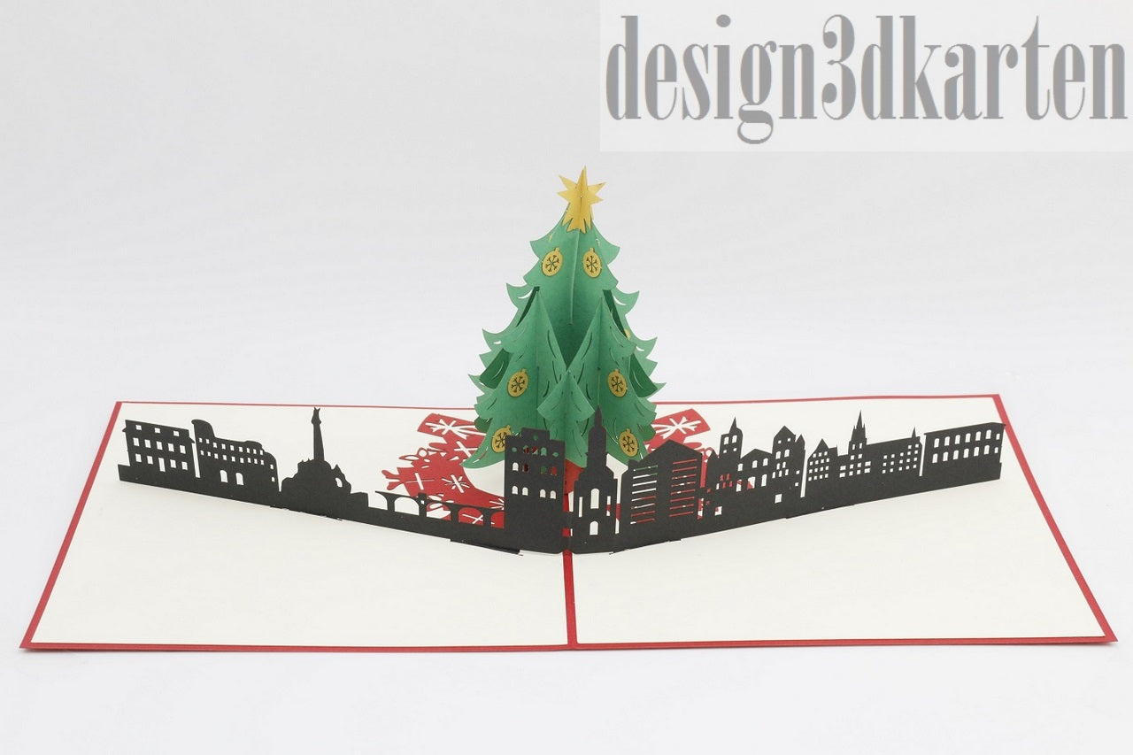 Aufgeklappte Pop-up-Karte mit Weihnachtsbaum vor der Skyline von Trier, seitlich fotografiert.
