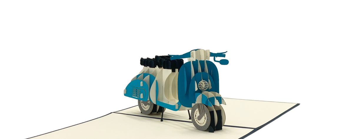 Aufgeklappte Pop-up-Karte mit einer blauen Vespa aus Papier, seitlich fotografiert.