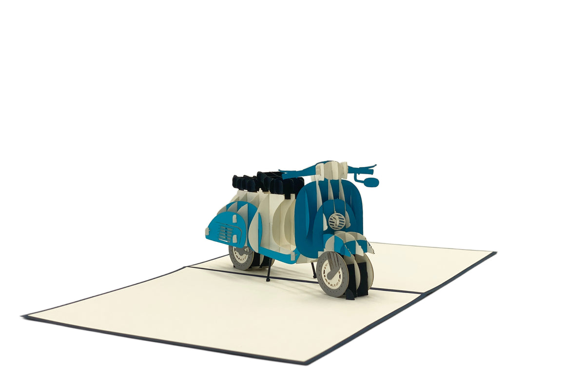 Aufgeklappte Pop-up-Karte mit einer blauen Vespa aus Papier, seitlich fotografiert.