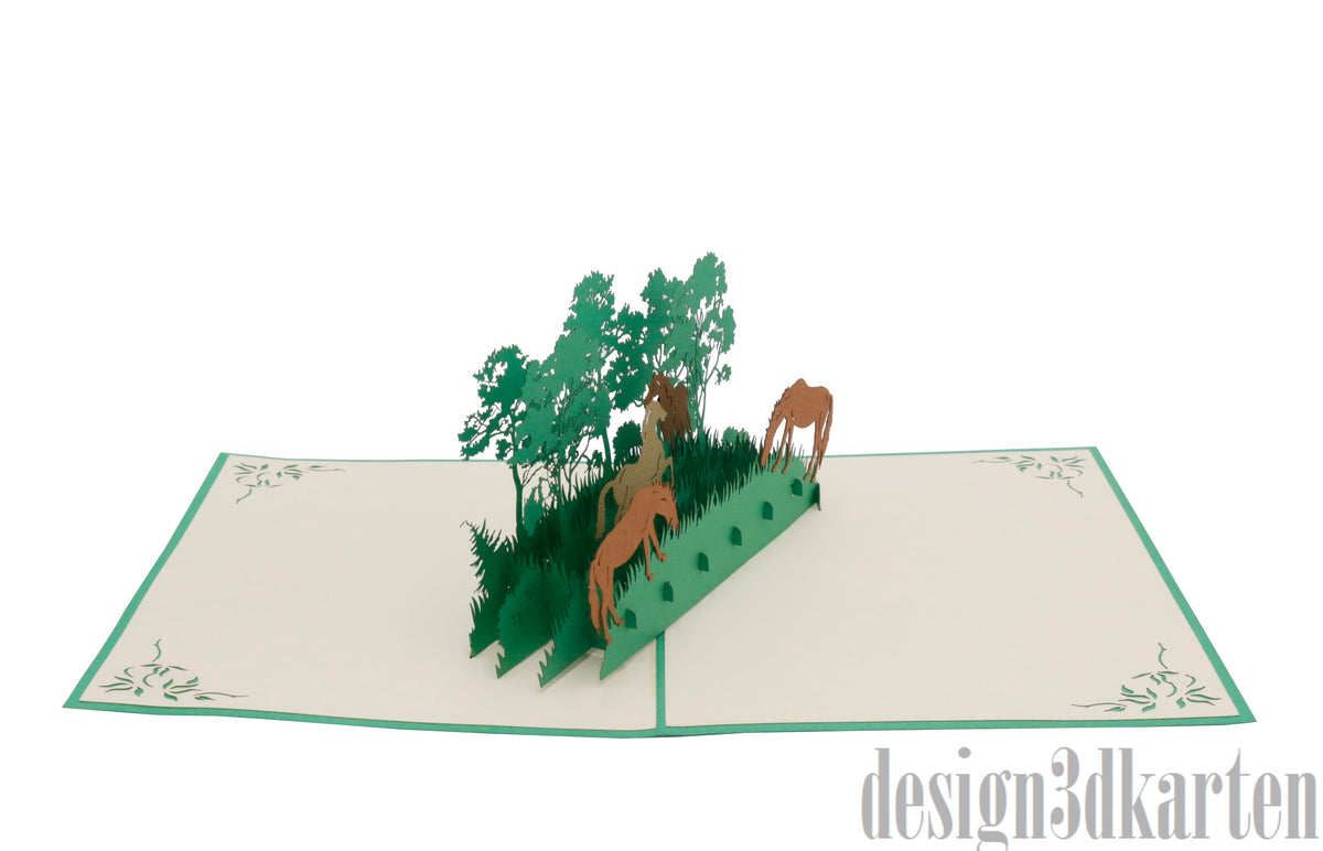 Aufgeklappte Pop-up-Karte mit Wildpferden und Bäumen aus Papier, schräg von der Seite fotografiert.