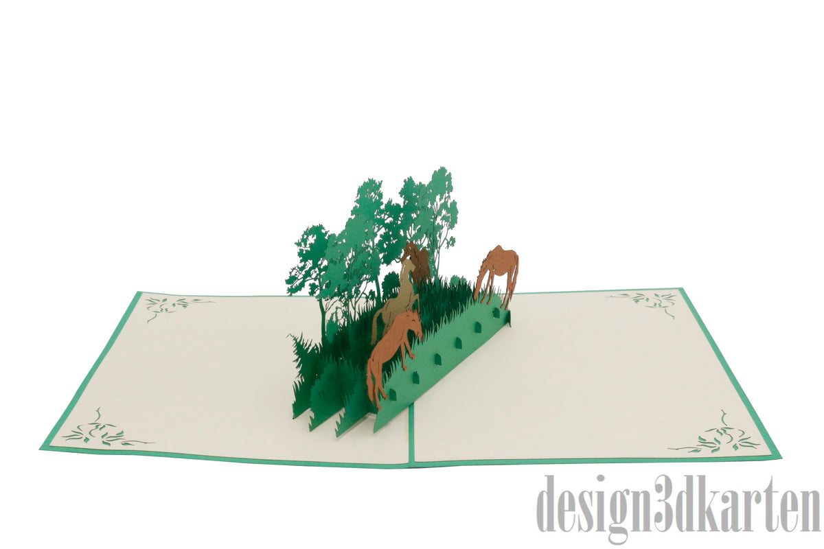 Aufgeklappte Pop-up-Karte mit Wildpferden und Bäumen aus Papier, schräg von der Seite fotografiert.