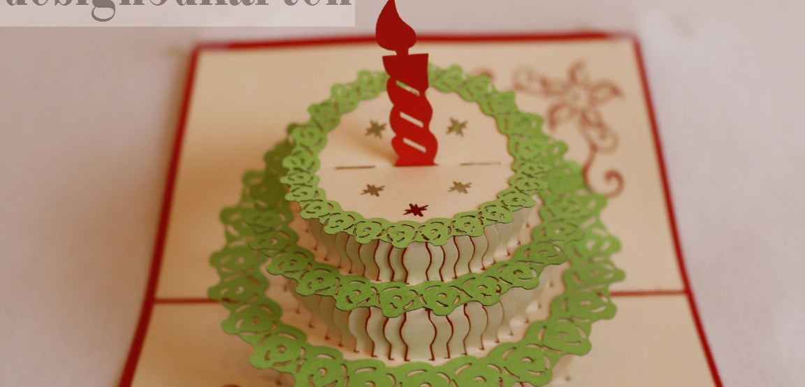 Nahaufnahme der aufgeklappten Pop-up-Karte mit einer Torte mit grünem Spitzendekor und roter Kerze.
