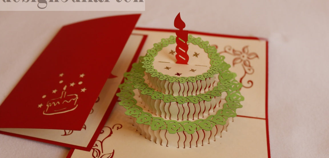 Aufgeklappte Pop-up-Karte mit einer Torte mit grünem Spitzendekor und roter Kerze, daneben die rote Kartenvorderseite.