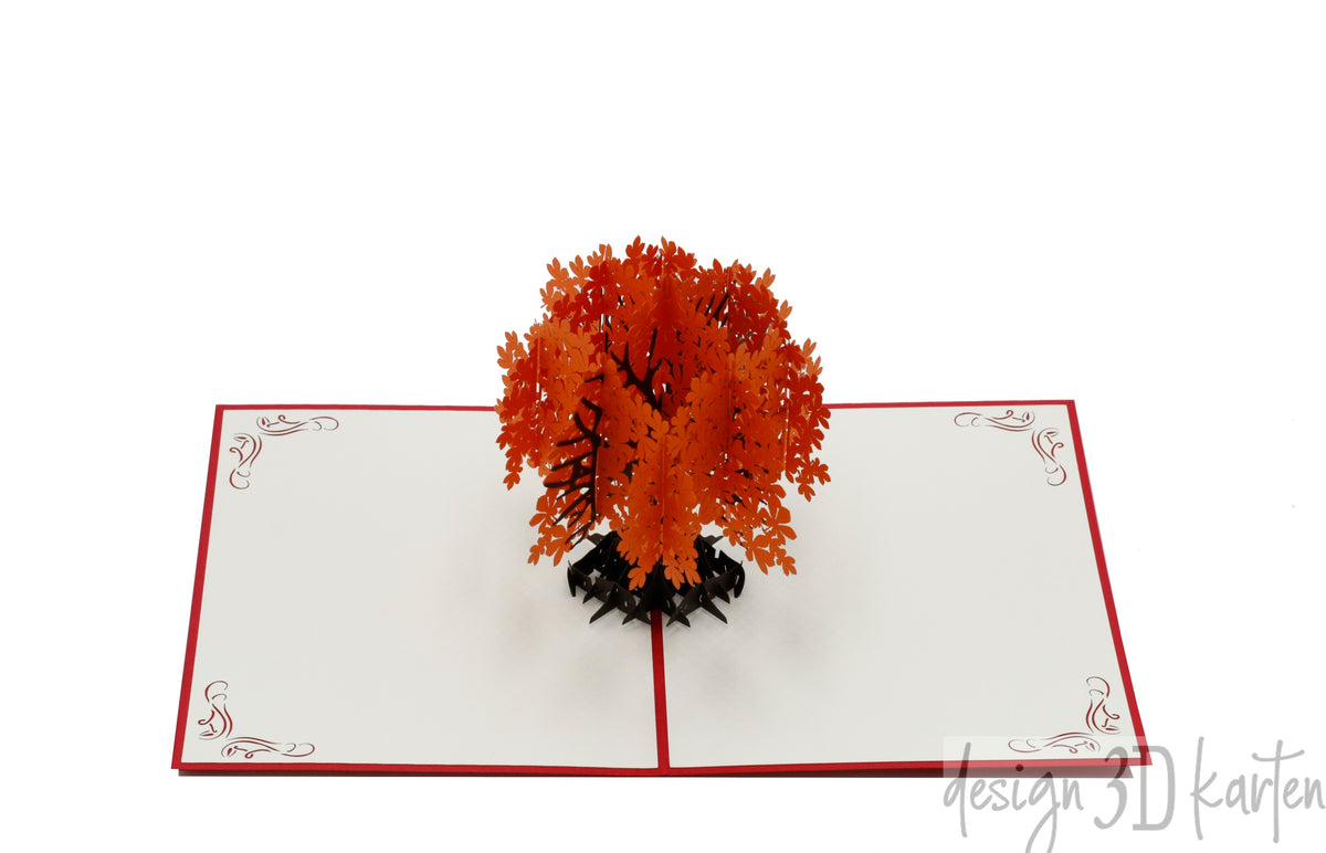 Aufgeklappte Pop-up-Karte mit orangefarbenem Herbstbaum, schräg von der Seite fotografiert.