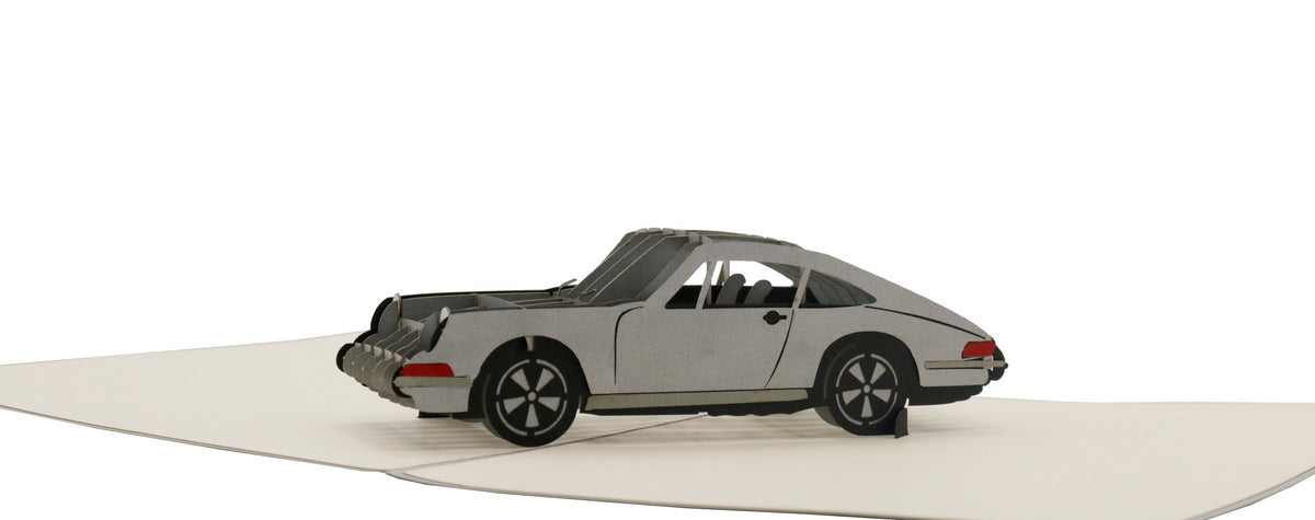 Aufgeklappte Pop-up-Karte mit einem silbernen Sportwagen aus Papier, seitlich fotografiert.