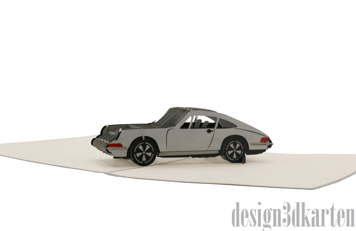 Aufgeklappte Pop-up-Karte mit einem silbernen Sportwagen aus Papier, seitlich fotografiert.