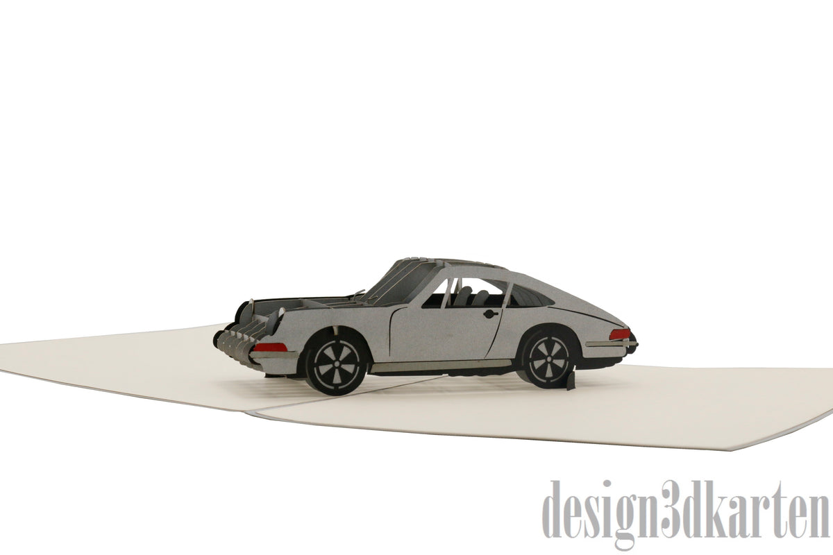 Aufgeklappte Pop-up-Karte mit einem silbernen Sportwagen aus Papier, seitlich fotografiert.