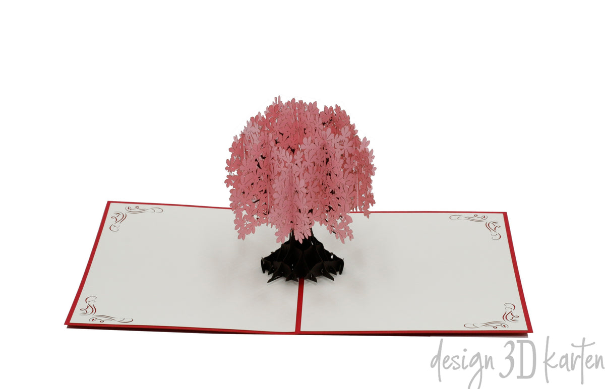 Aufgeklappte Pop-up-Karte mit rosa Blütenbaum aus Papier, seitlich fotografiert.