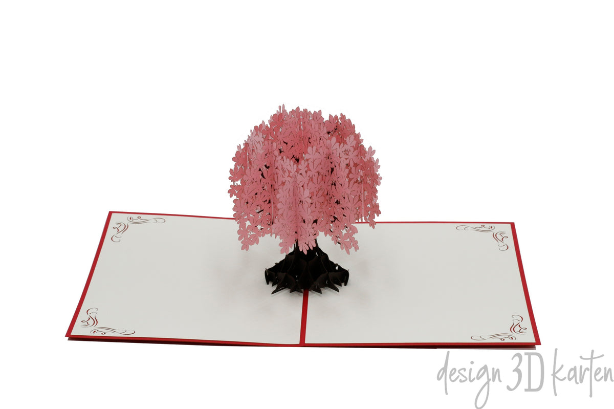 Aufgeklappte Pop-up-Karte mit rosa Blütenbaum aus Papier, seitlich fotografiert.