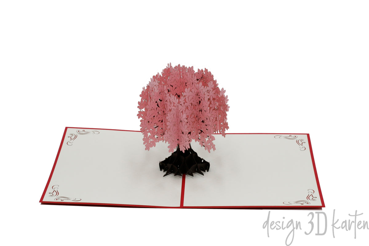 Aufgeklappte Pop-up-Karte mit rosa Blütenbaum aus Papier, seitlich fotografiert.