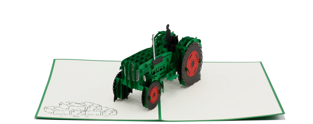 Aufgeklappte Pop-up-Karte mit grünem Oldtimer-Traktor aus Papier, seitlich fotografiert.