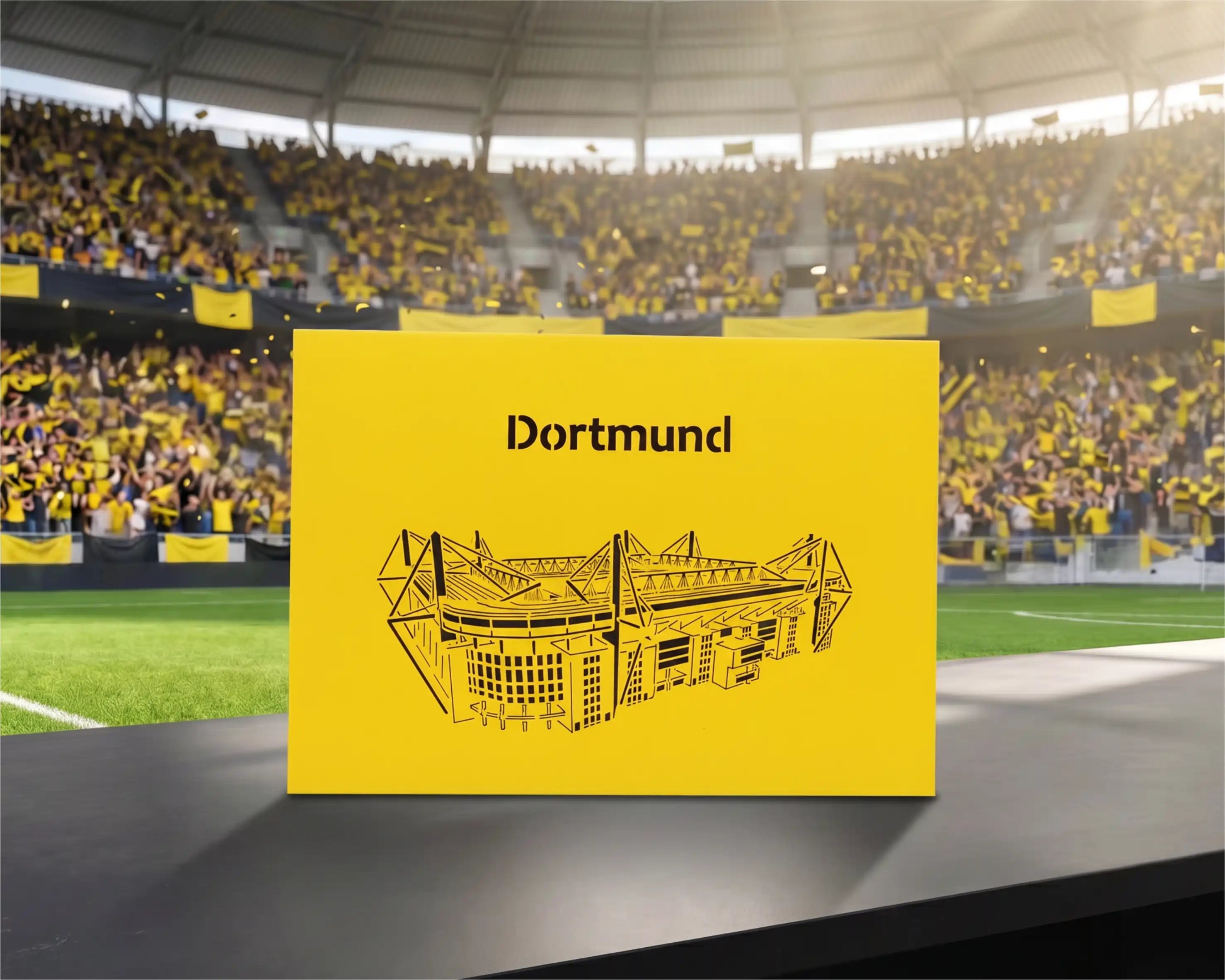 Gelbe Pop-up-Karte mit schwarzem Scherenschnitt eines Stadions und dem Schriftzug Dortmund auf einem Tisch im Fußballstadion.