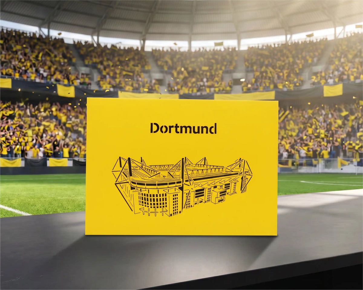 Gelbe Pop-up-Karte mit schwarzem Scherenschnitt eines Stadions und dem Schriftzug Dortmund auf einem Tisch im Fußballstadion.