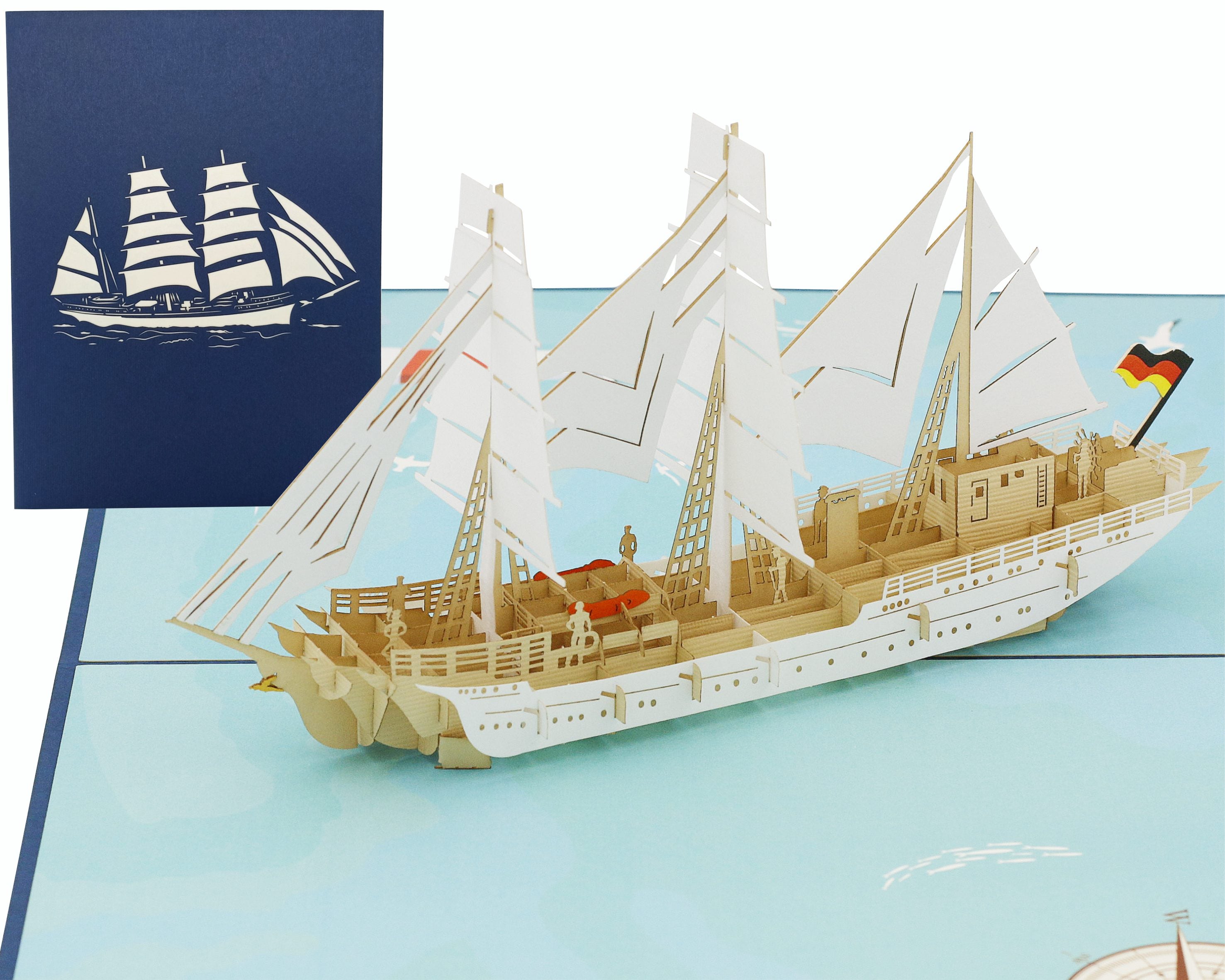 Aufgeklappte Pop-up-Karte mit dem Segelschiff Gorch Fock und Deutschlandflagge, dahinter die blaue Kartenvorderseite mit Segelschiff-Scherenschnitt.