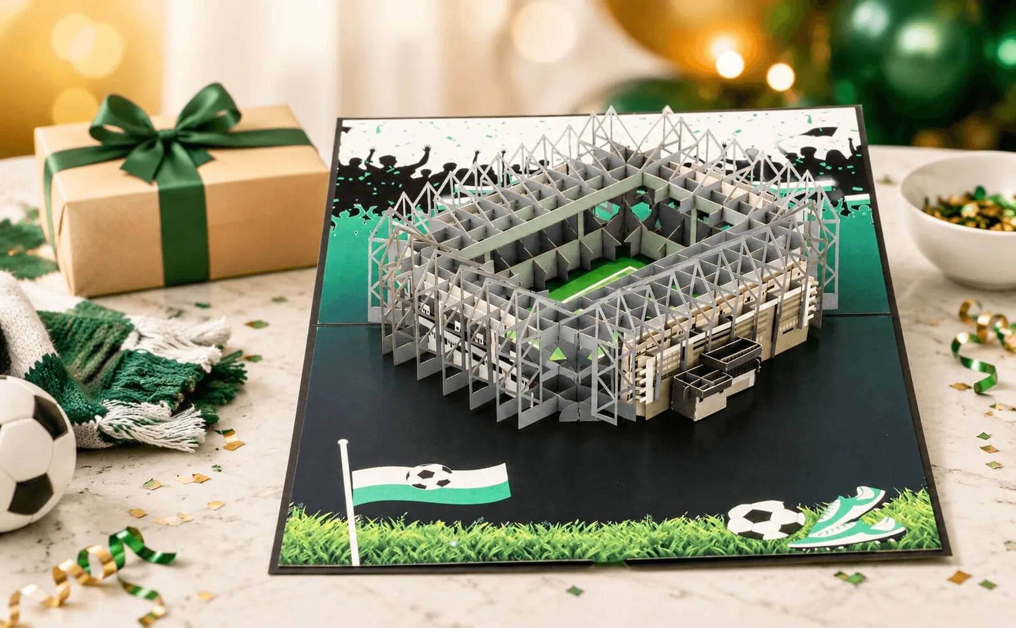 Aufgeklappte Pop-up-Karte zum Geburtstag mit detailreichem Stadionmodell, grün-weißem Rasenmuster und Fußballmotiven auf einem Tisch mit Geschenk und Dekoration