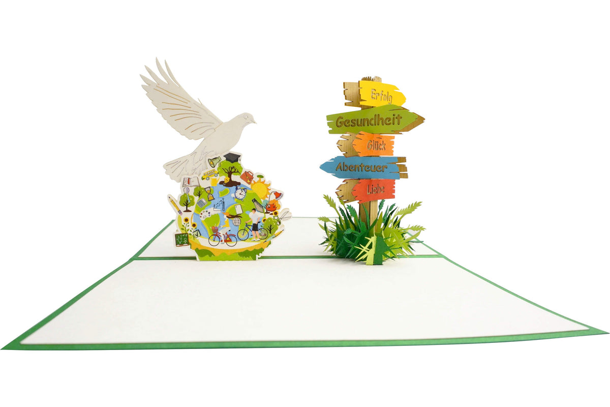 Aufgeklappte Pop-up-Karte mit weißer Friedenstaube über einer bunten Weltkugel, daneben ein Wegweiser mit den Schildern Erfolg, Gesundheit, Glück, Abenteuer und Liebe.