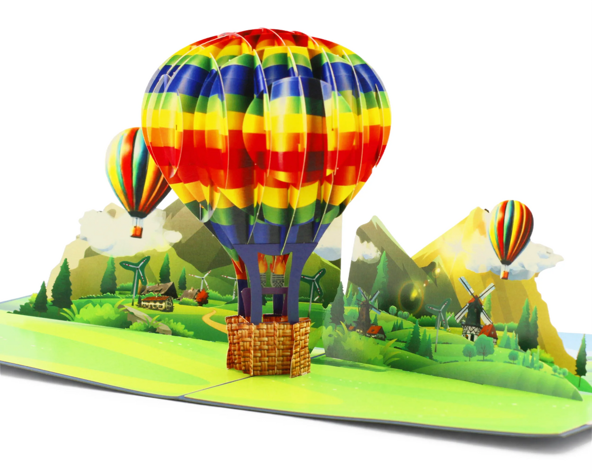 Aufgeklappte 3D Pop-up Karte mit großem regenbogenfarbenem Heißluftballon über einer Berglandschaft mit Windmühlen und zwei kleinen Ballons