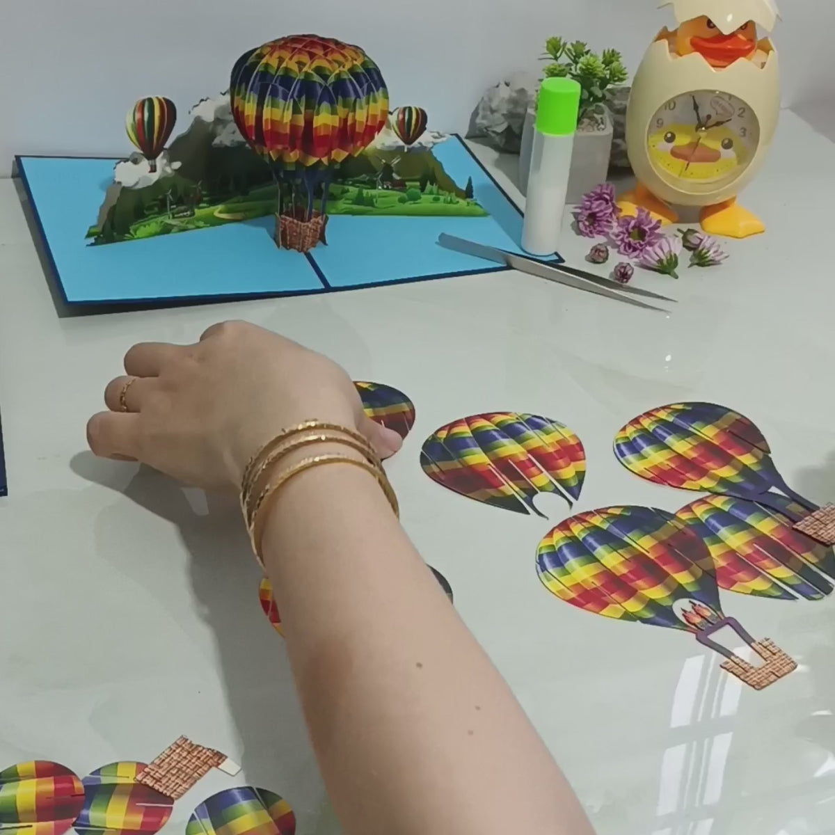 Video: Aufgeklappte Pop-up-Karte mit buntem Heißluftballon, daneben die einzelnen Papierteile des Ballons.