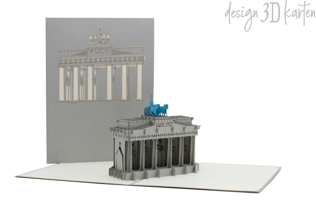 Aufgeklappte Pop-up-Karte mit dem Brandenburger Tor, dahinter die graue Kartenvorderseite mit Brandenburger-Tor-Scherenschnitt.