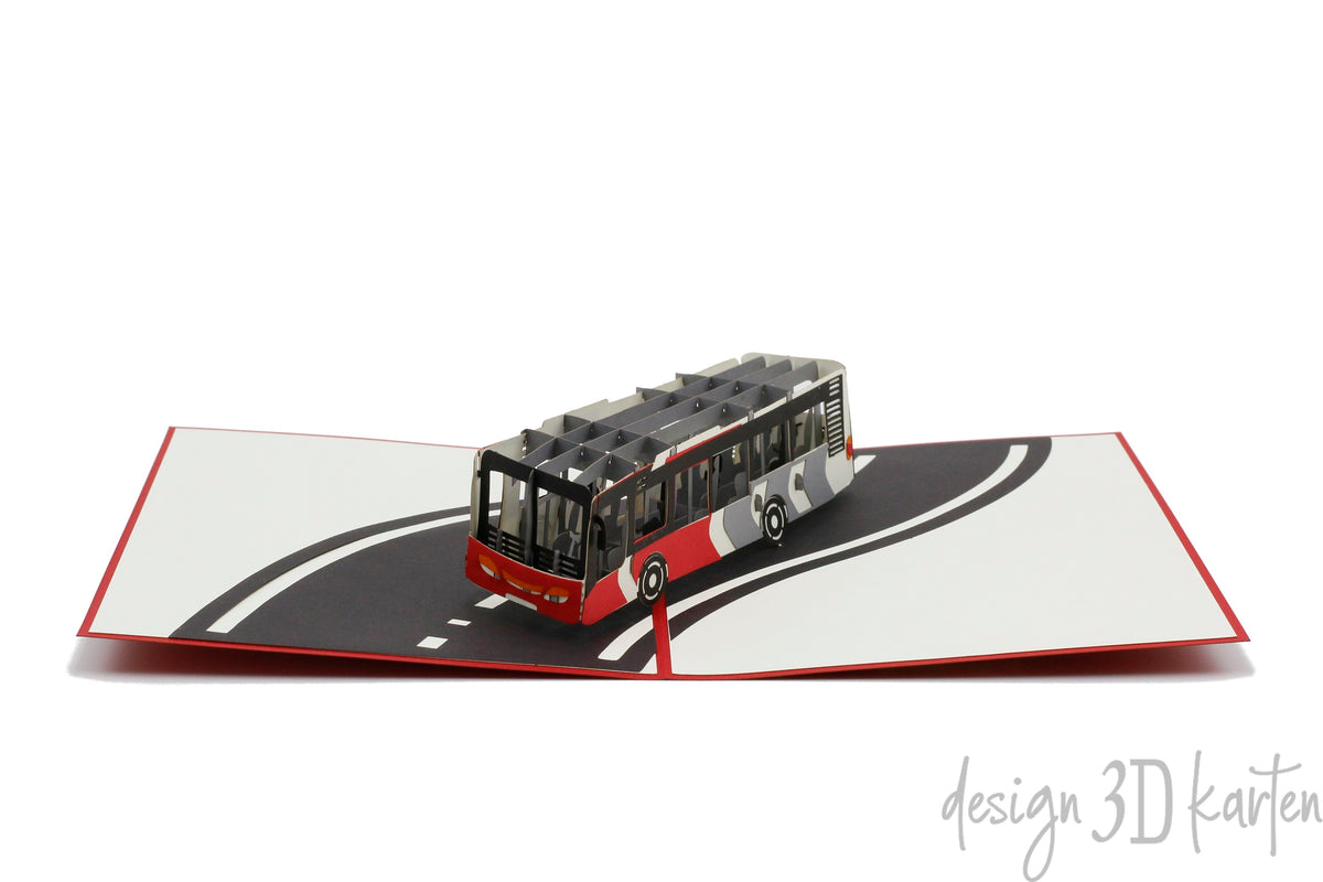 Aufgeklappte Pop-up-Karte mit einem Linienbus auf einer geschwungenen Straße, schräg von oben fotografiert.