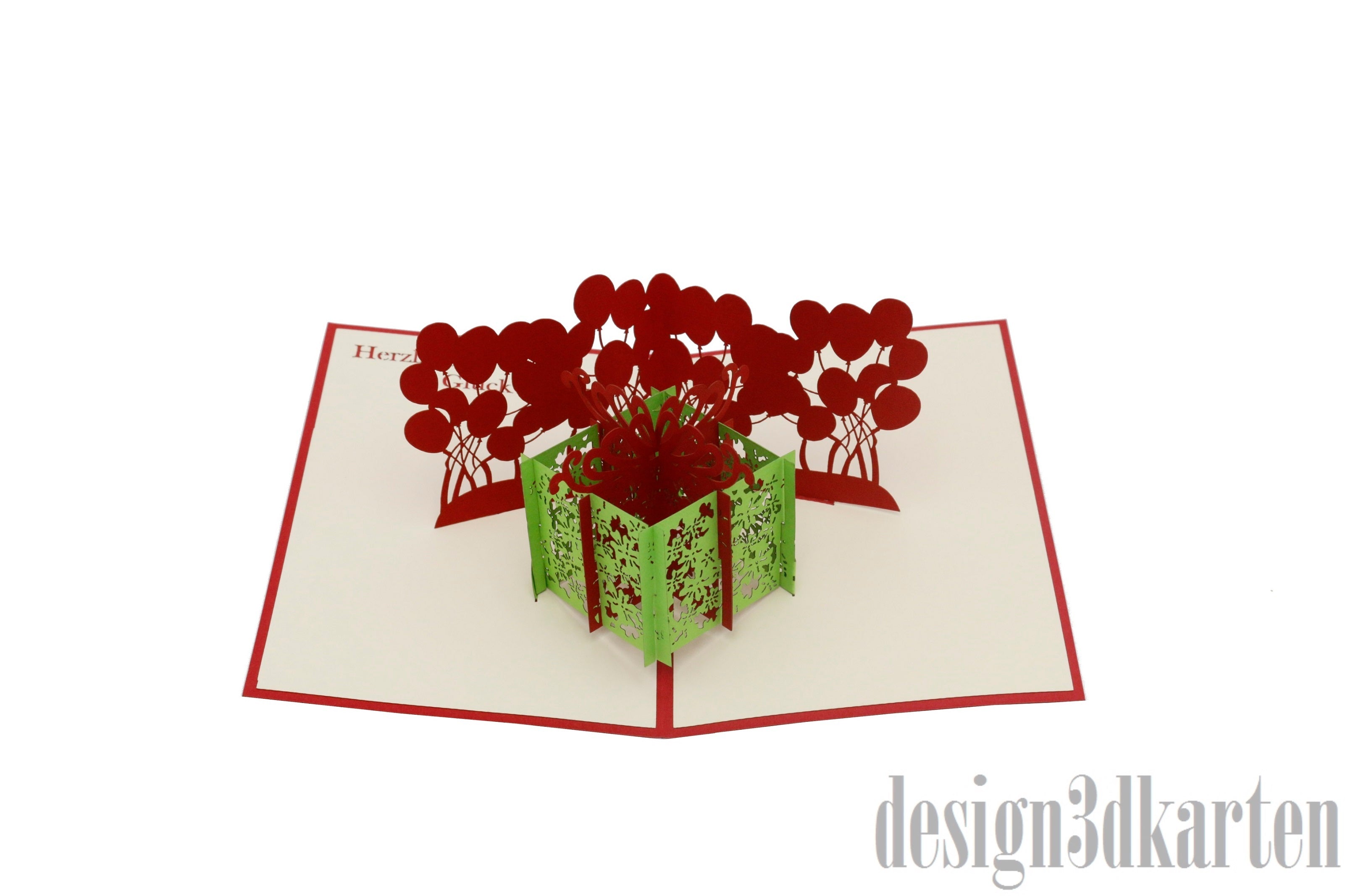 Aufgeklappte Pop-up-Karte mit grüner Geschenkbox und roten Luftballons, frontal fotografiert.