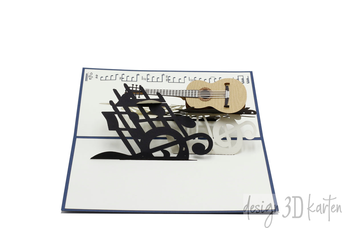 Aufgeklappte Pop-up-Karte mit dunkelblauem Rand: eine Gitarre neben einem schwarzen Notenschlüssel und Notenlinien.