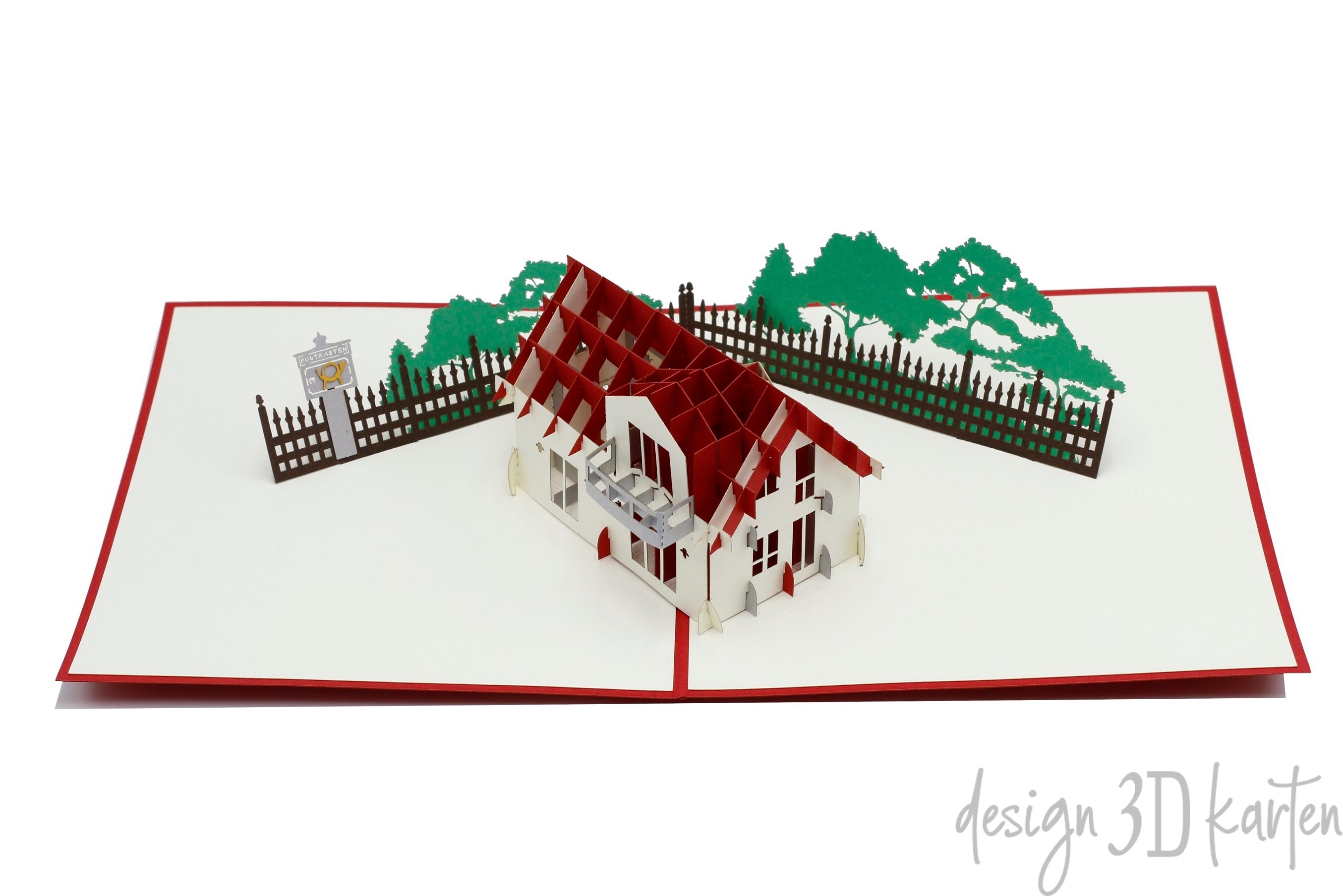 Aufgeklappte Pop-up-Karte mit rotem Rand: ein Haus mit rotem Dach, Gartenzaun und Bäumen.