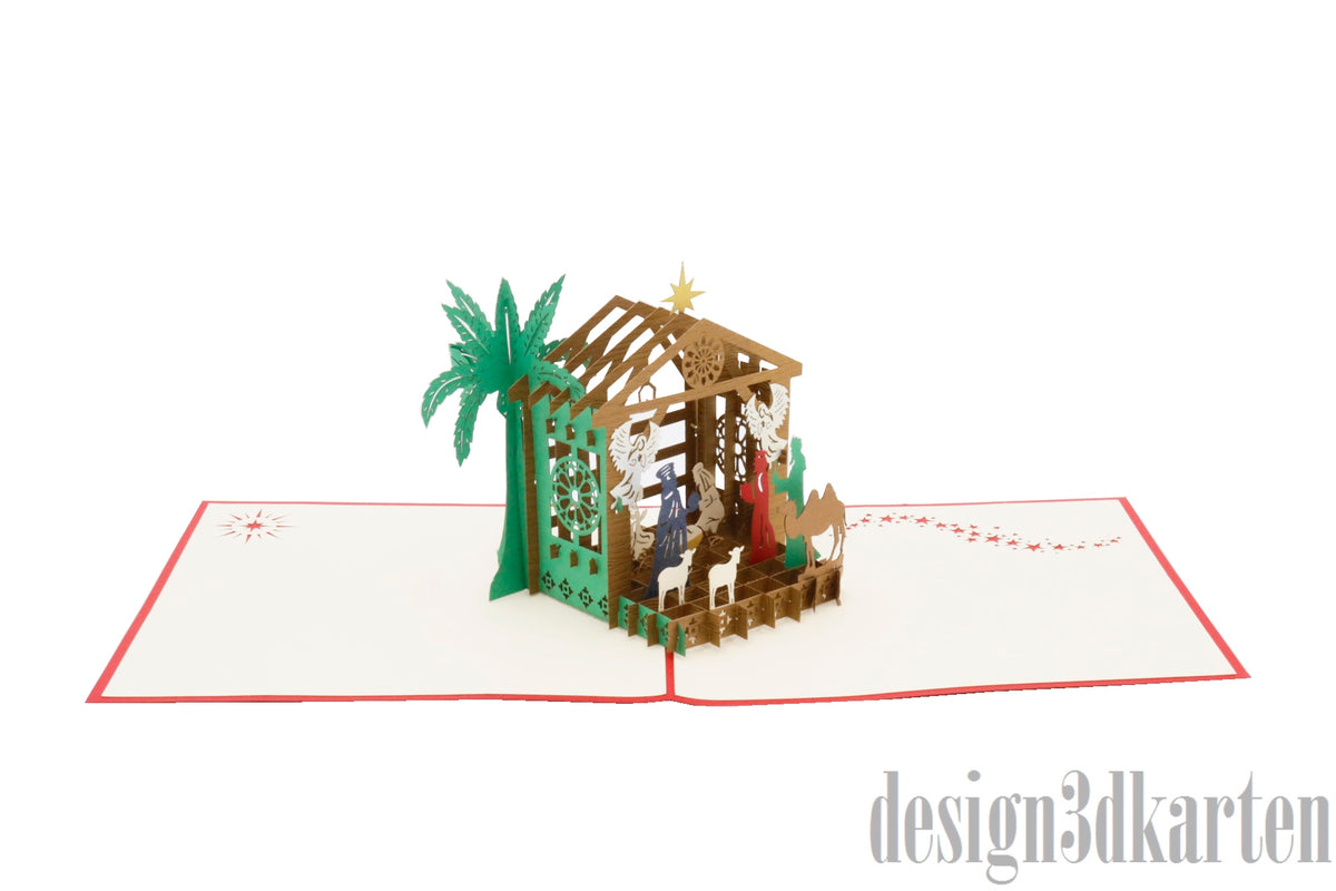Aufgeklappte Pop-up-Karte mit Weihnachtskrippe und Palme aus Papier, schräg von der Seite fotografiert.