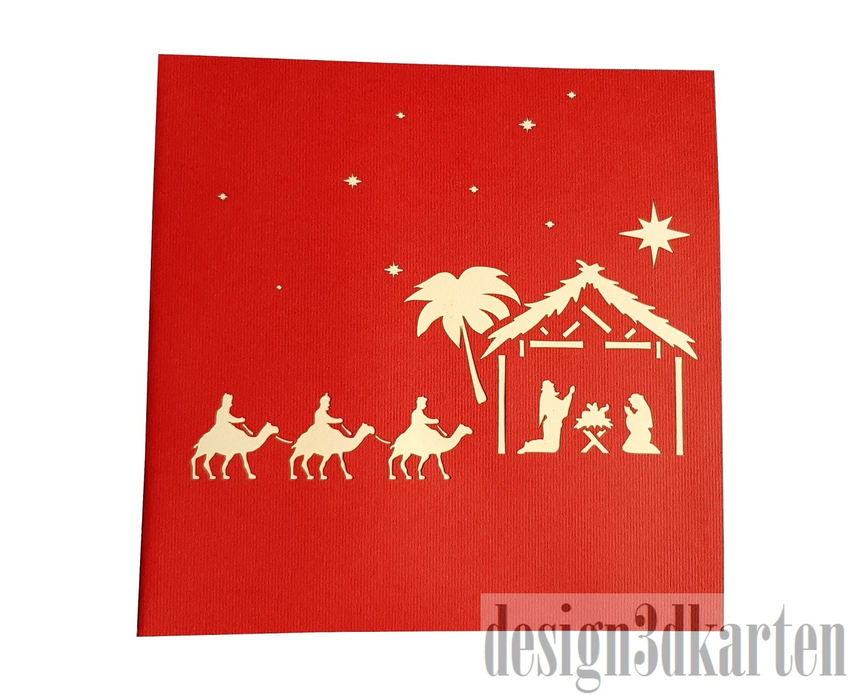 Rote Kartenvorderseite mit Weihnachtskrippe, den Heiligen Drei Königen auf Kamelen und dem Stern als Scherenschnitt.