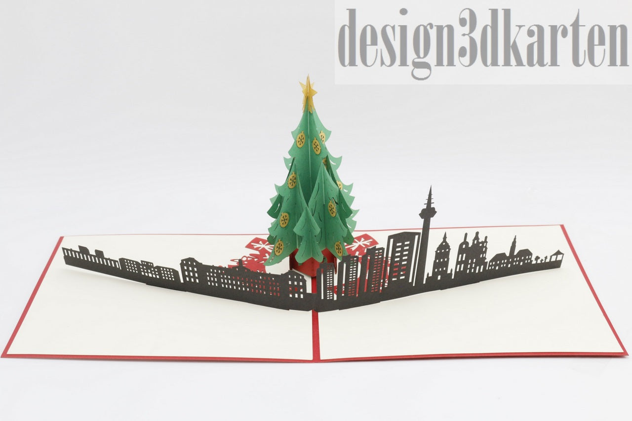 Aufgeklappte Pop-up-Karte mit Weihnachtsbaum vor der Skyline von Mannheim, schräg von der Seite fotografiert.