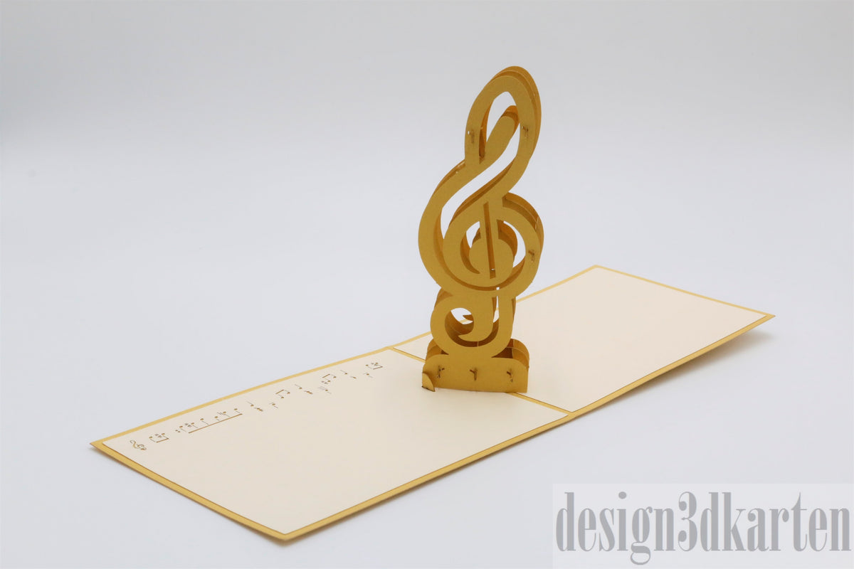 Aufgeklappte cremefarbene Pop-up-Karte mit einem goldenen Violinschlüssel und Notenlinien.