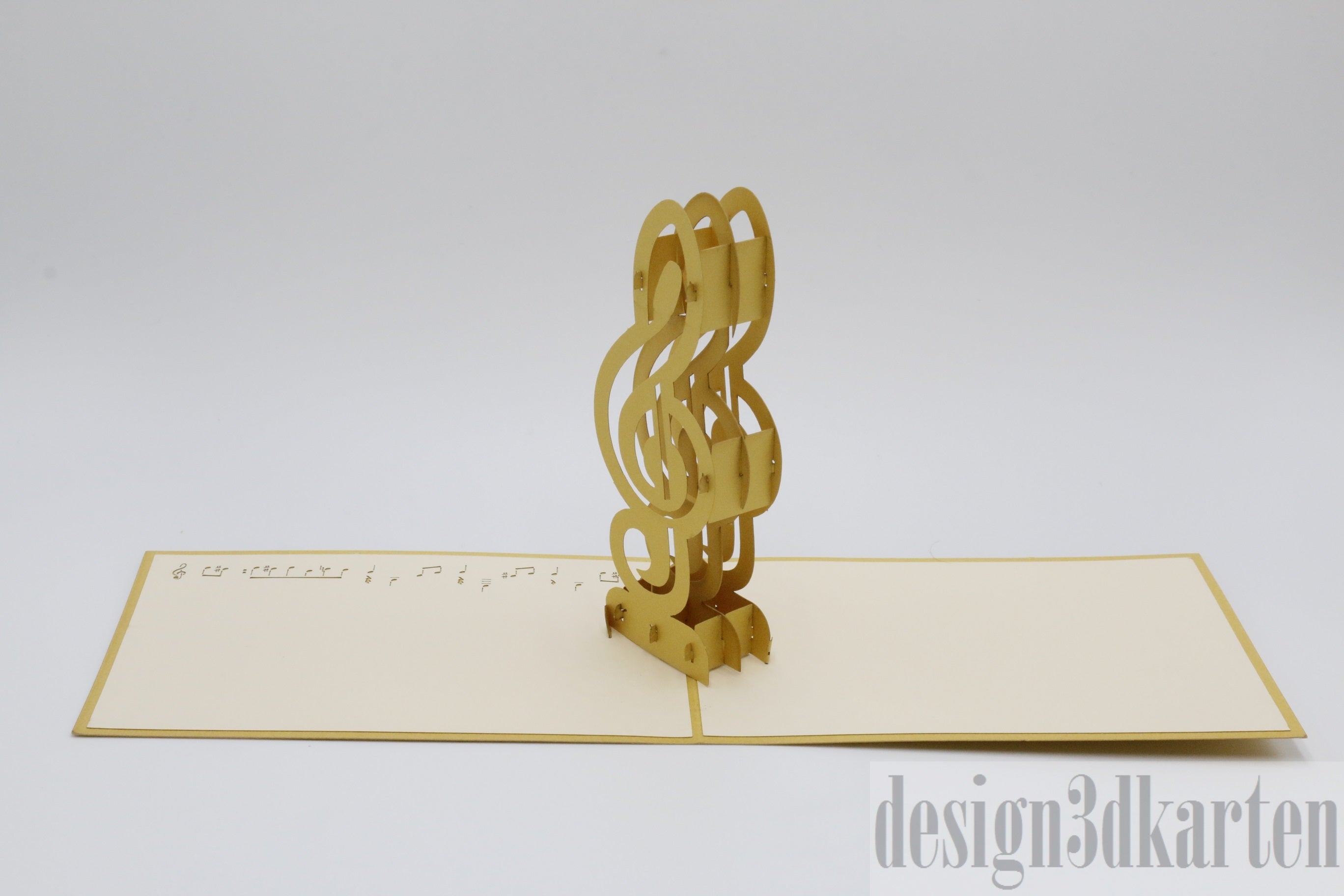 Aufgeklappte Pop-up-Karte mit einem goldenen Violinschlüssel auf einem Notenblatt, schräg fotografiert.