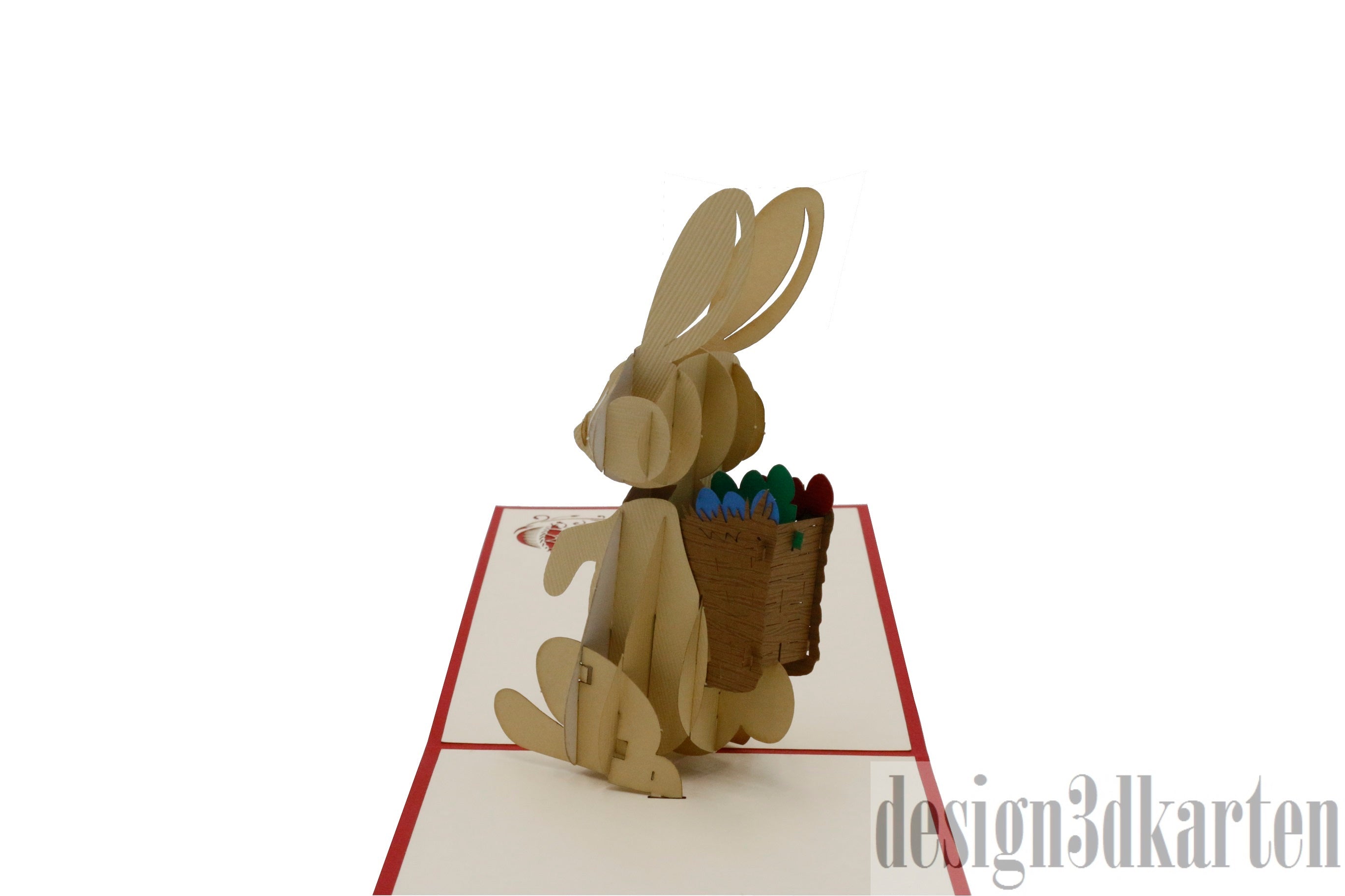 Aufgeklappte Pop-up-Karte mit Osterhase und Eierkorb aus Papier, schräg von der Seite fotografiert.