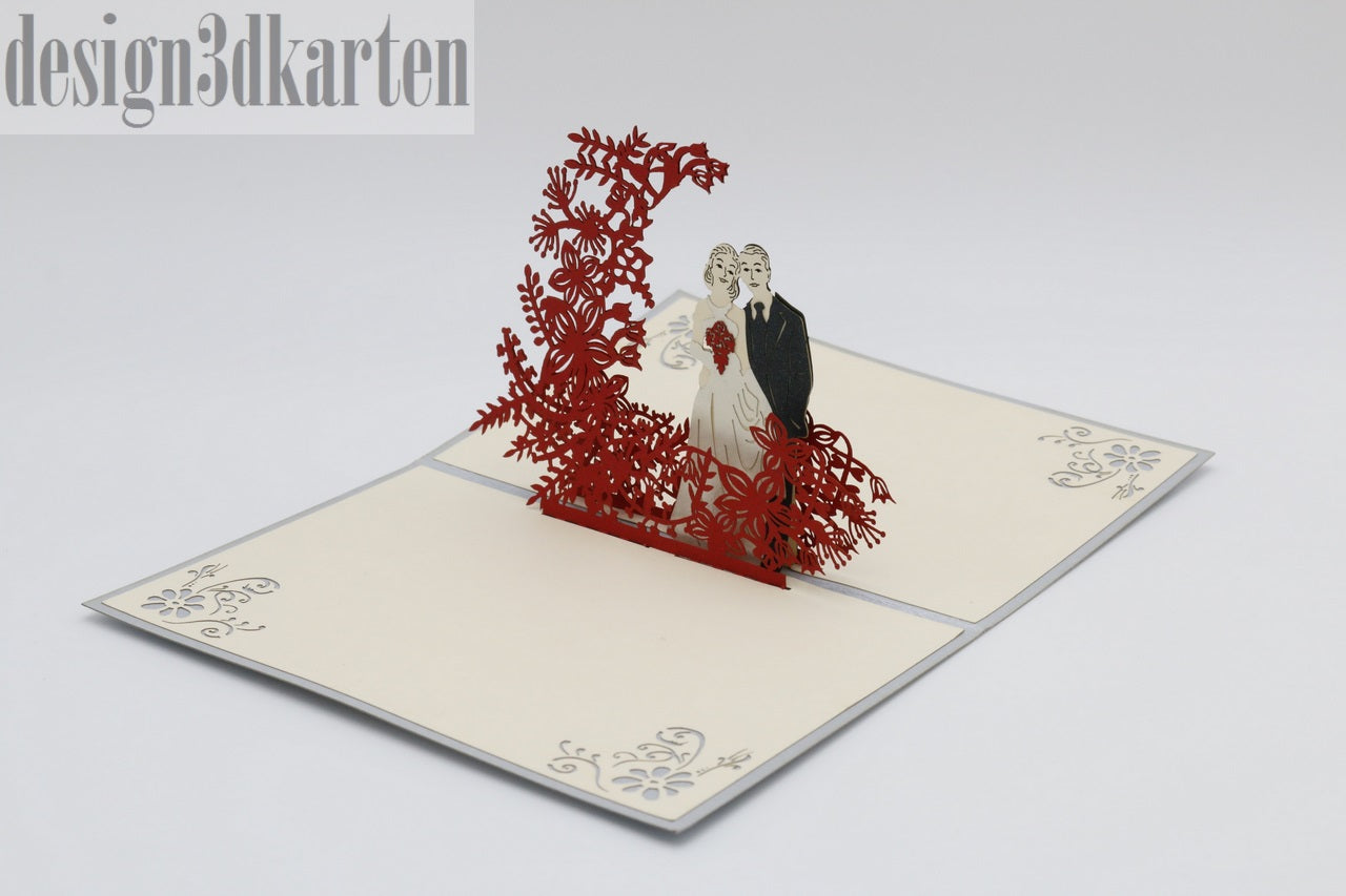 Aufgeklappte Pop-up-Karte mit einem Hochzeitspaar vor einem roten Blütenbogen, seitlich fotografiert.
