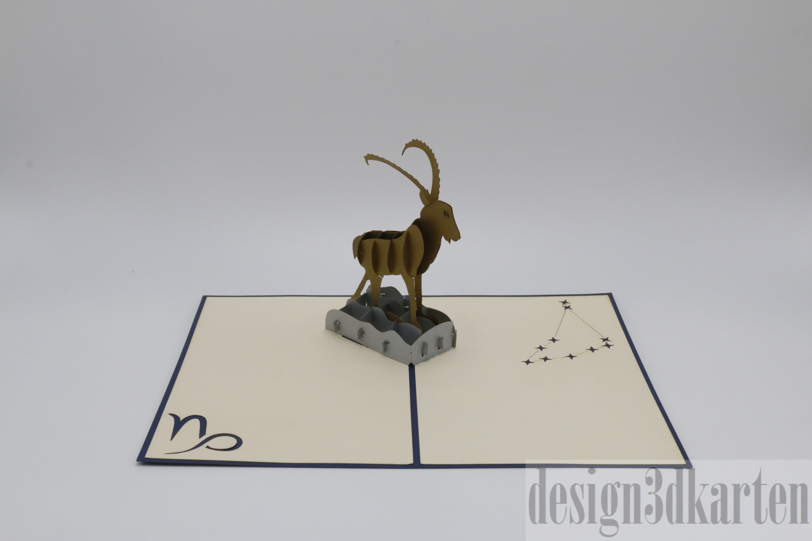 Aufgeklappte Pop-up-Karte mit goldenem Steinbock auf einem Felsen, daneben Symbol und Sternbild Steinbock.