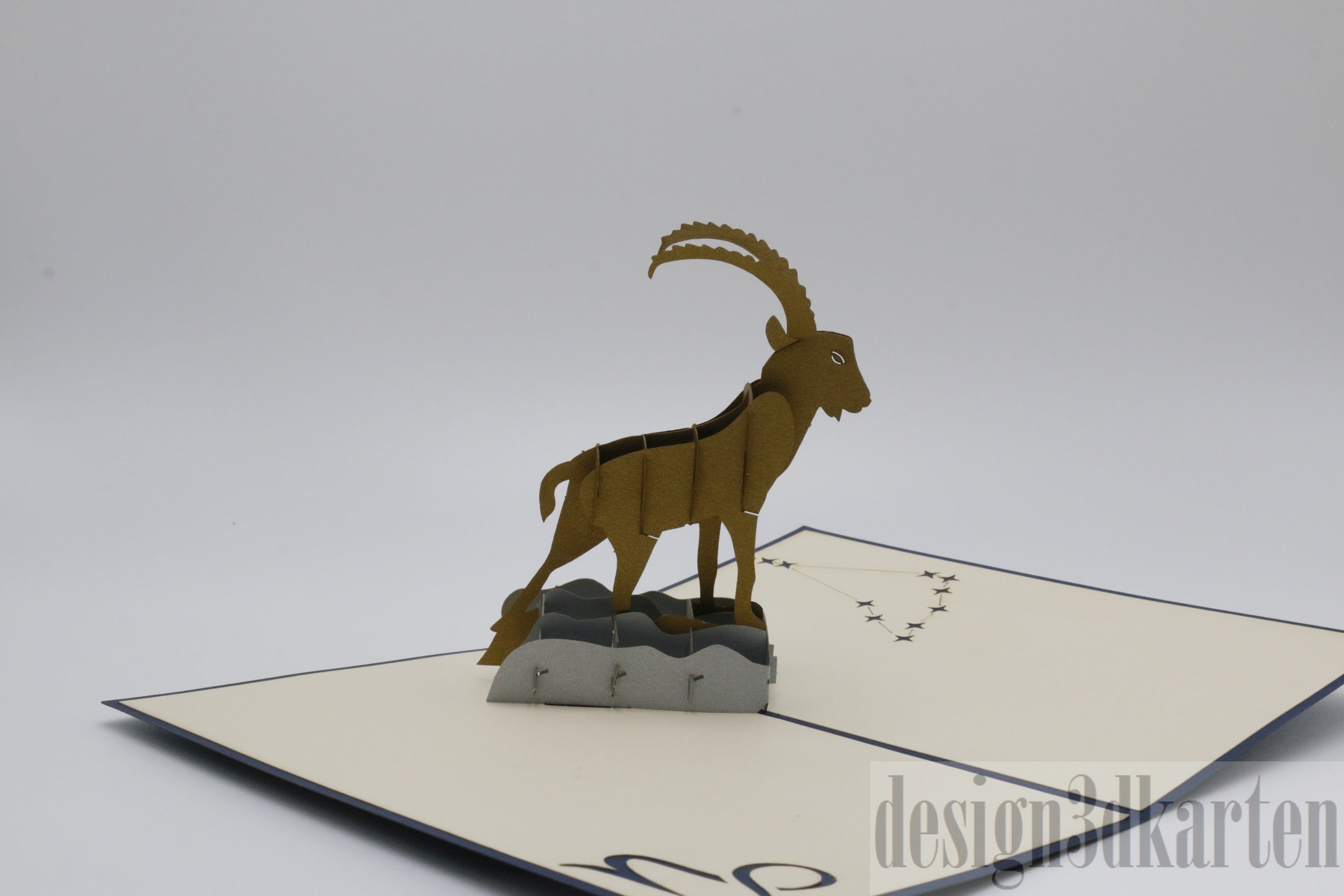 Aufgeklappte Pop-up-Karte mit einem goldenen Steinbock auf einem Felsen, seitlich fotografiert.